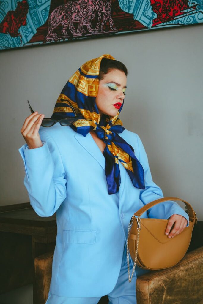 Stylish woman in blue suit and scarf holding a chic handbag indoors.